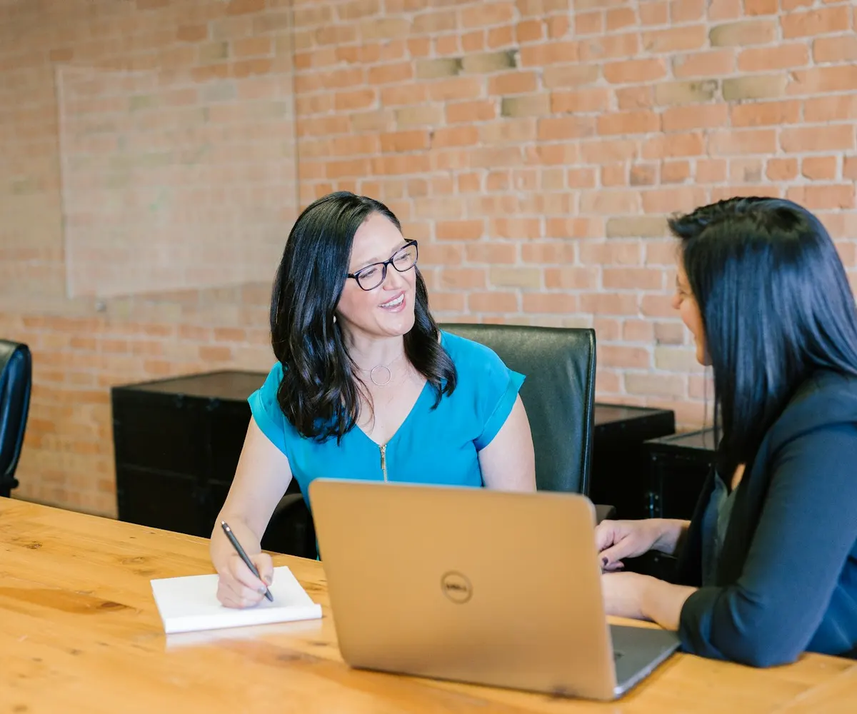 Two people in conversation across a table during a working consultation.
