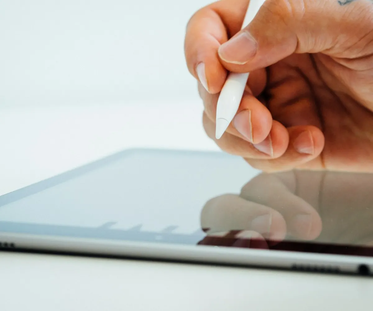 A hand holding a stylus above a tablet screen.